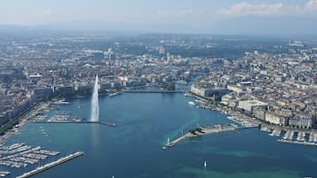 Une vue urbaine mettant en valeur un plan d’eau important, avec une fontaine centrale, entouré de bâtiments urbains denses et d’un port de plaisance où sont amarrés de nombreux bateaux.