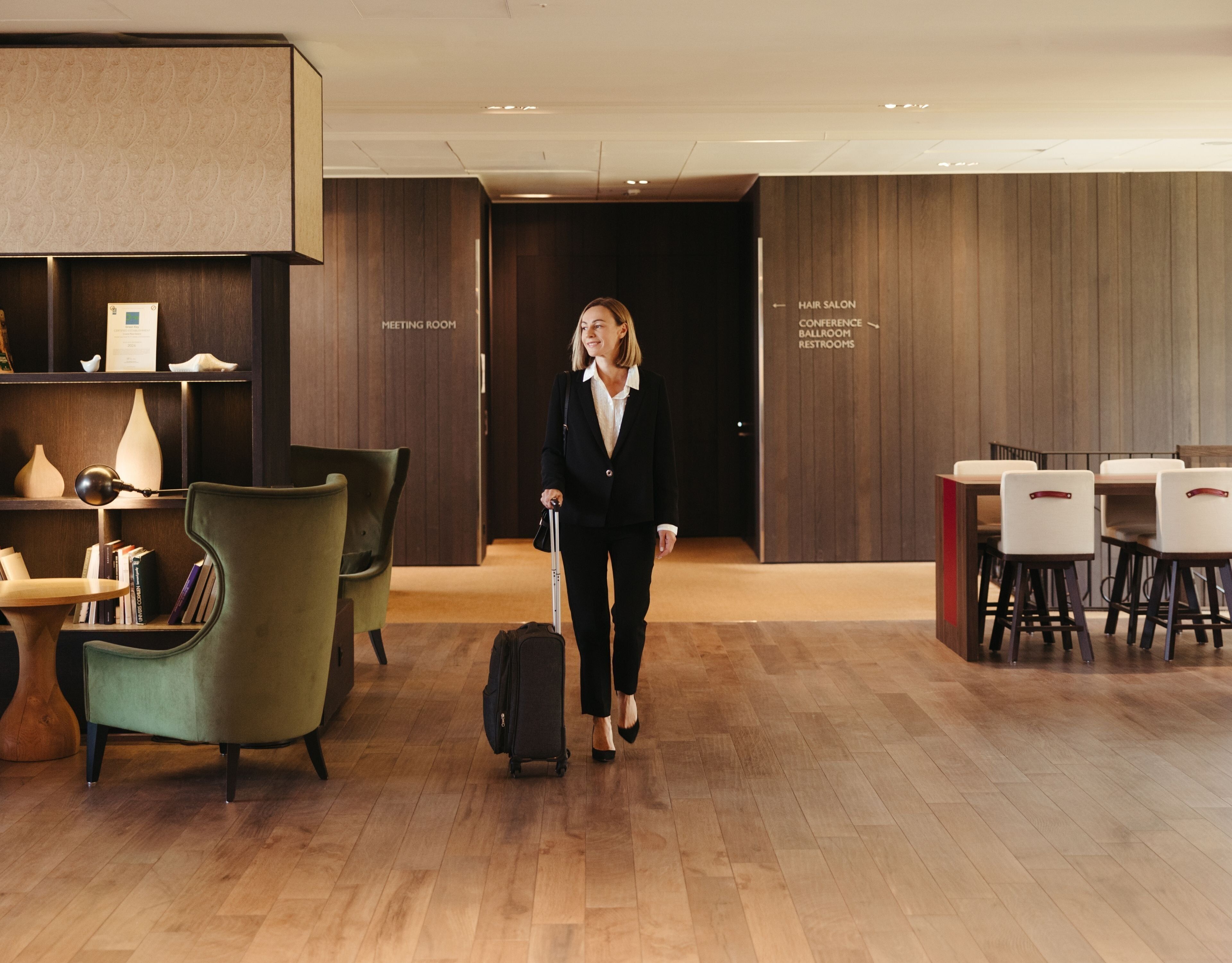 Un moderno vestíbulo de hotel con piso de madera, un sillón verde, una sala de reuniones y una peluquería.