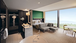 A modern hotel room with a large bed, a sofa, a dining table, and a view of the mountains. - Crowne Plaza Geneva by IHG (Meyrin)