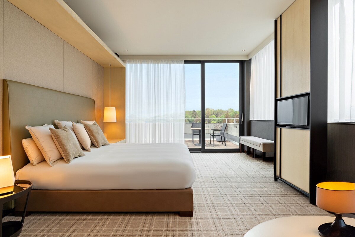 Una habitación de hotel moderna con una cama grande, televisión y un balcón con vistas.