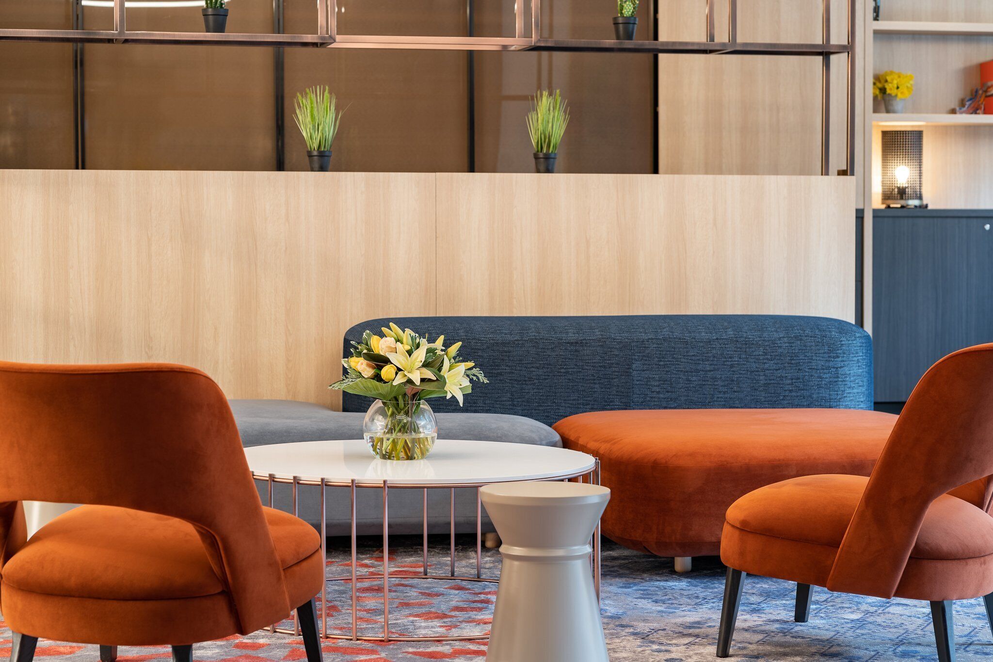 A modern lounge area with orange chairs, a round white table, and a blue sofa.