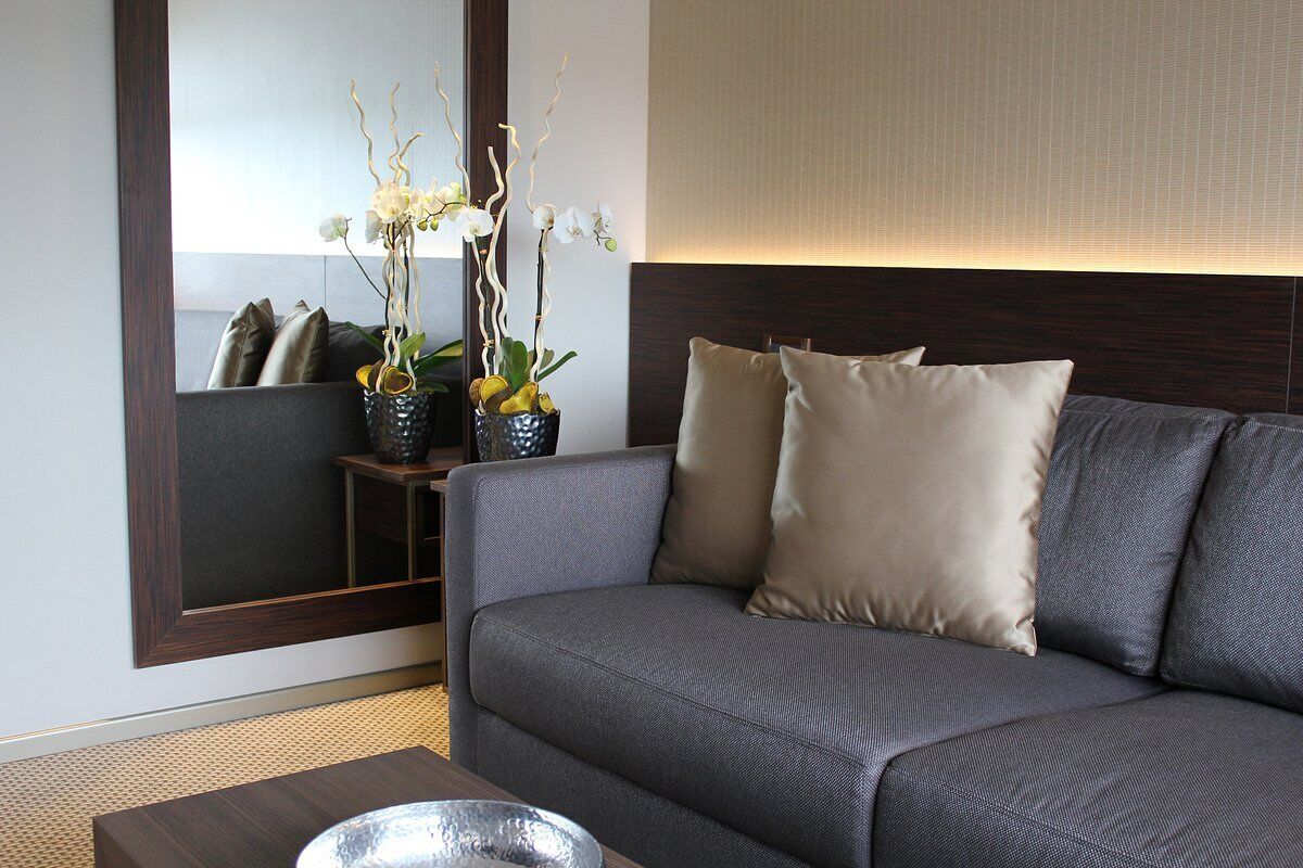 Ein modernes Wohnzimmer mit einem grauen Sofa, zwei beigen Kissen, einem kleinen Beistelltisch und einer dekorativen Orchideen-Anordnung.