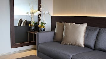 Ein modernes Wohnzimmer mit einem grauen Sofa, zwei beigen Kissen, einem kleinen Beistelltisch und einer dekorativen Orchideen-Anordnung.