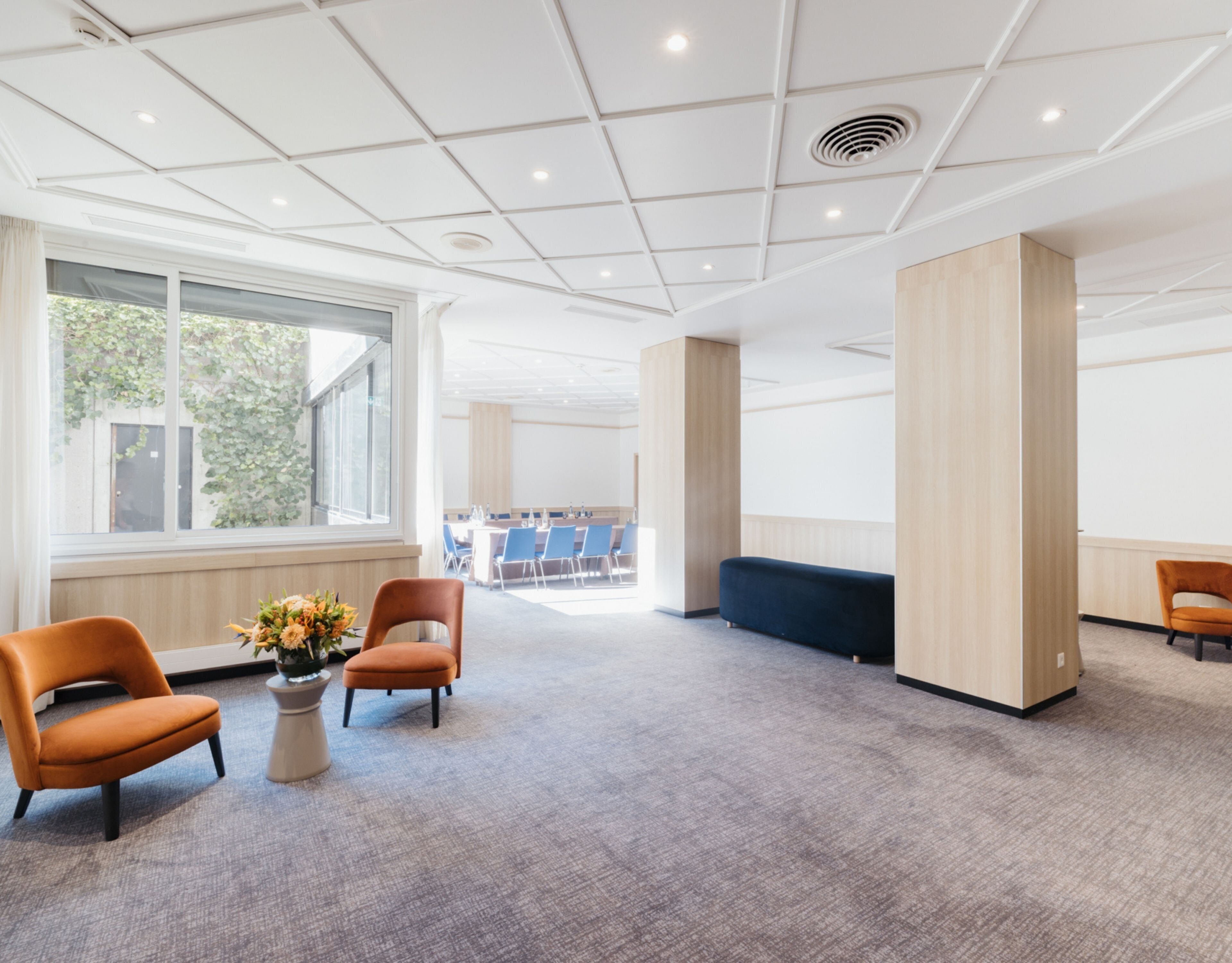 A spacious lobby with a high ceiling, large windows, and a seating area with chairs and a sofa.