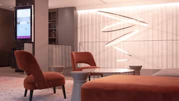 Habitación de hotel moderna con una televisión de pantalla plana grande, sillas tapizadas en naranja, una mesa redonda y una lámpara de techo original.