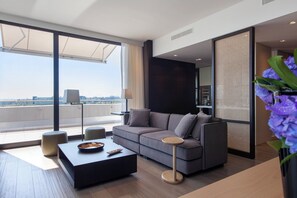 A modern living room with a sectional sofa, a coffee table, and a view of the city. - Crowne Plaza Geneva by IHG (Meyrin)
