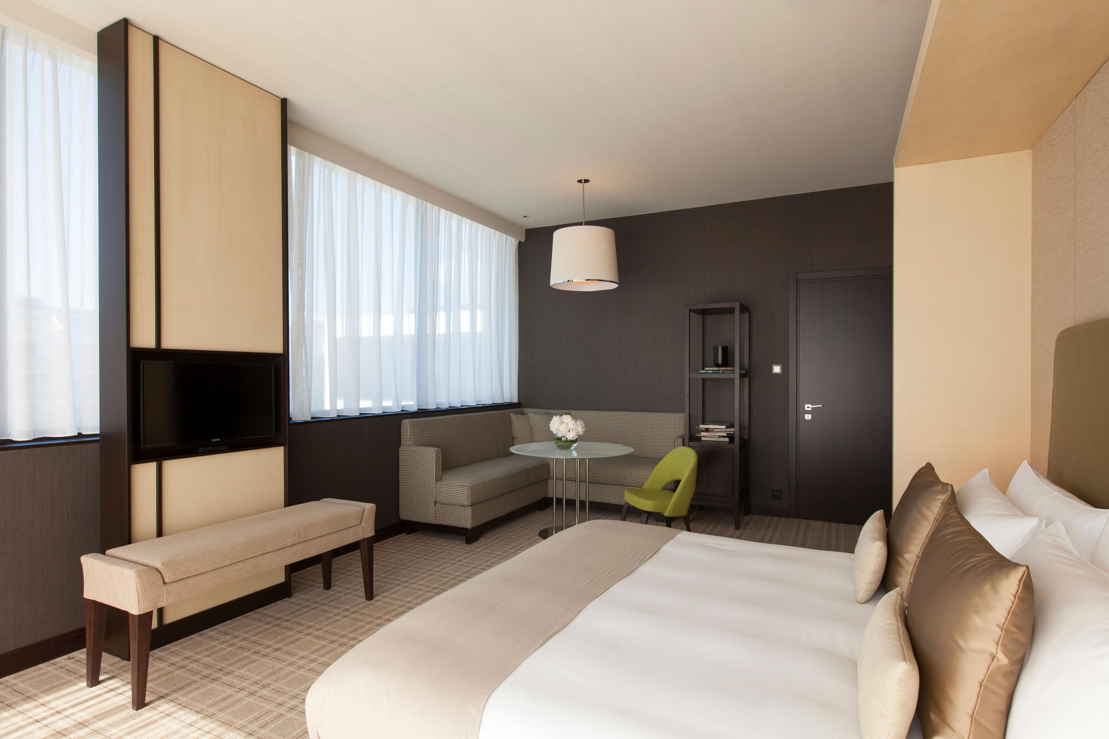 A hotel room with a large bed, a bench, a sofa, a small table, a TV, and a door.
