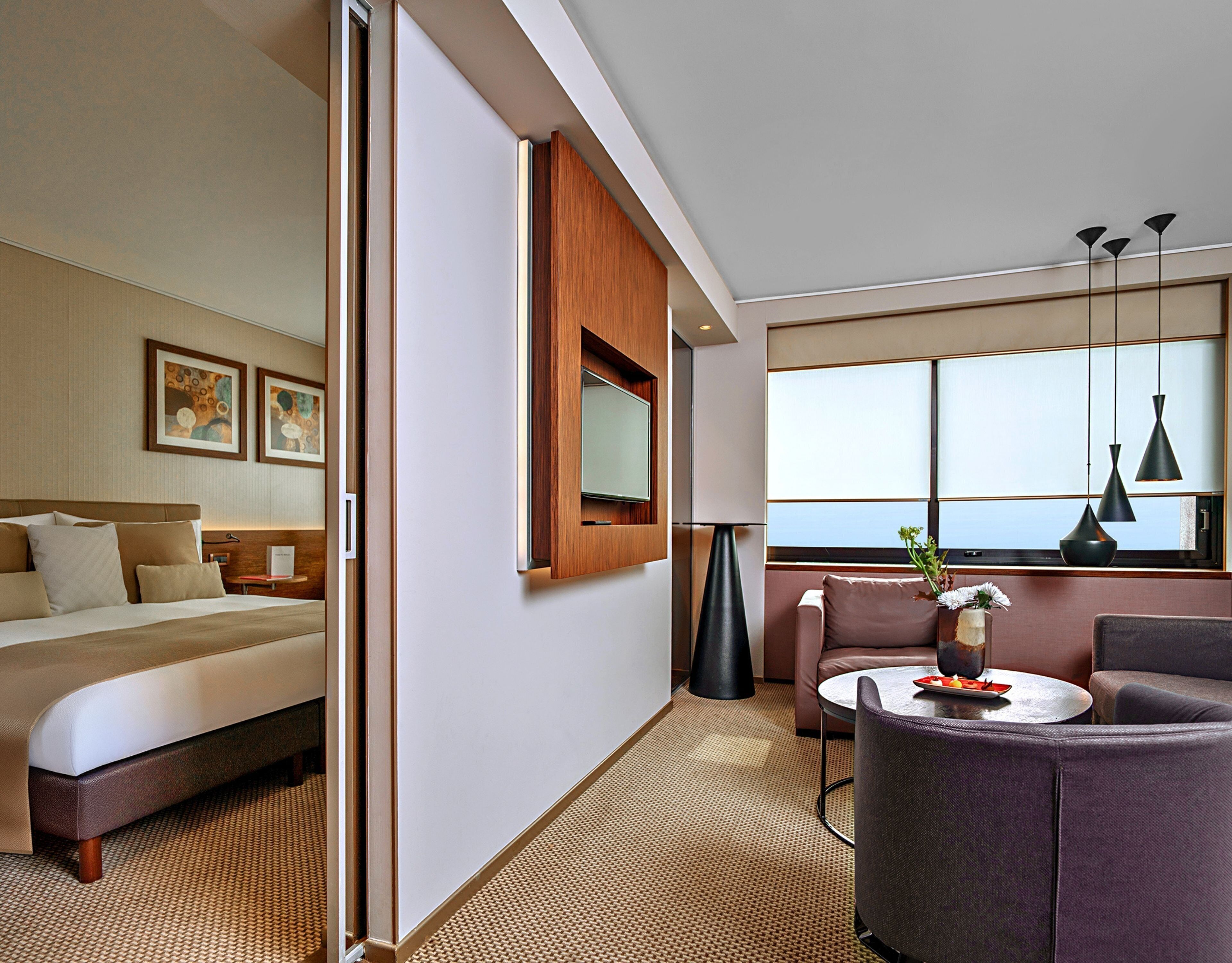 A hotel room with a bed, a sofa, a small table, a potted plant, and a large window.