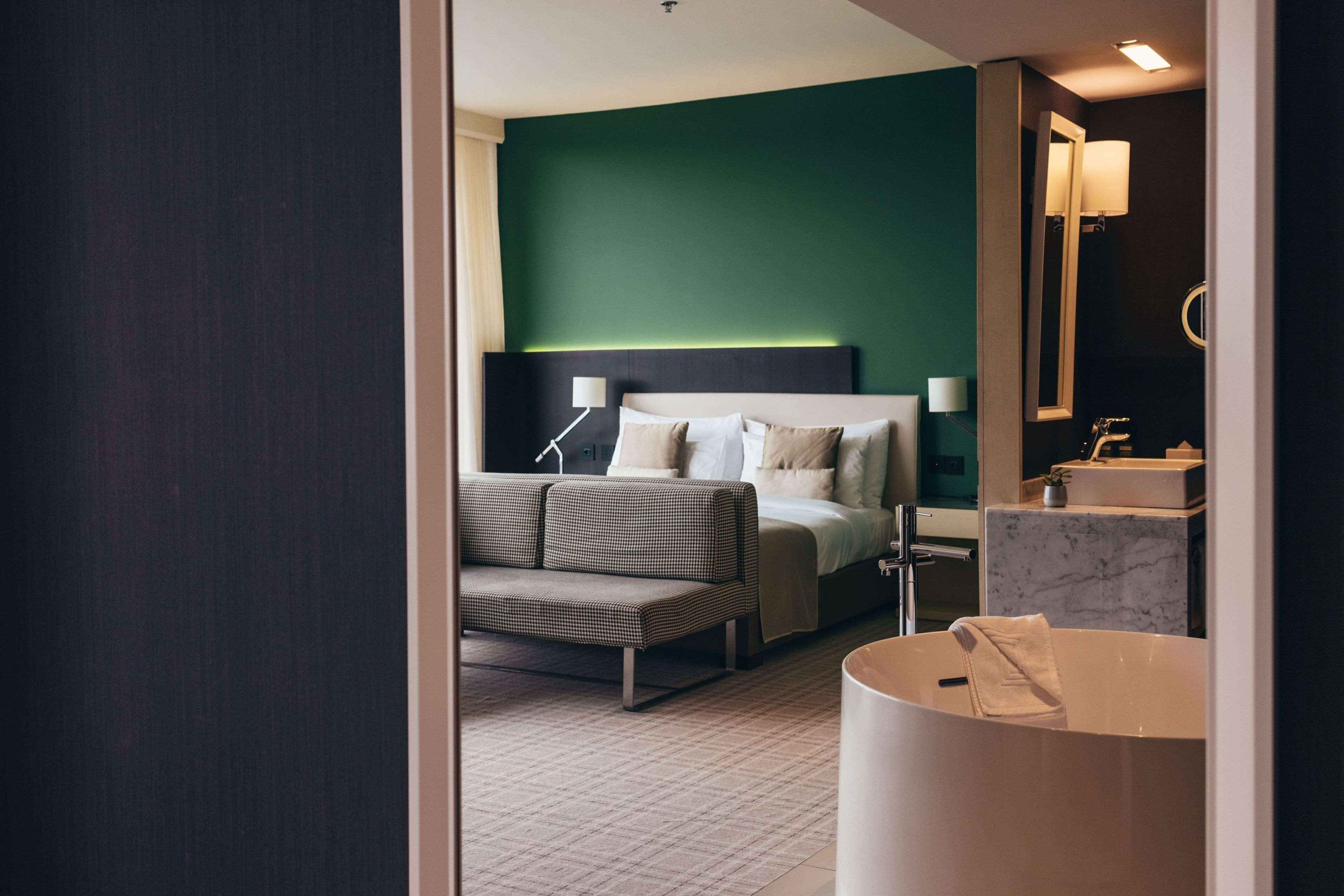 Habitación de hotel con cama, sofá, baño con lavamanos y espejo, y una bañera grande.