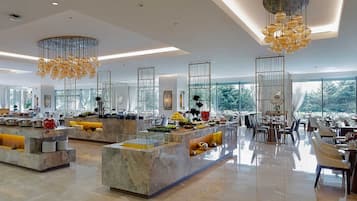 A spacious hotel lobby with marble counters, modern chandeliers, and large windows offering a view of the outdoors.