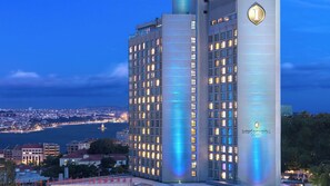 Um hotel imponente com vários andares, grandes janelas e um painel de luz vertical marcante.