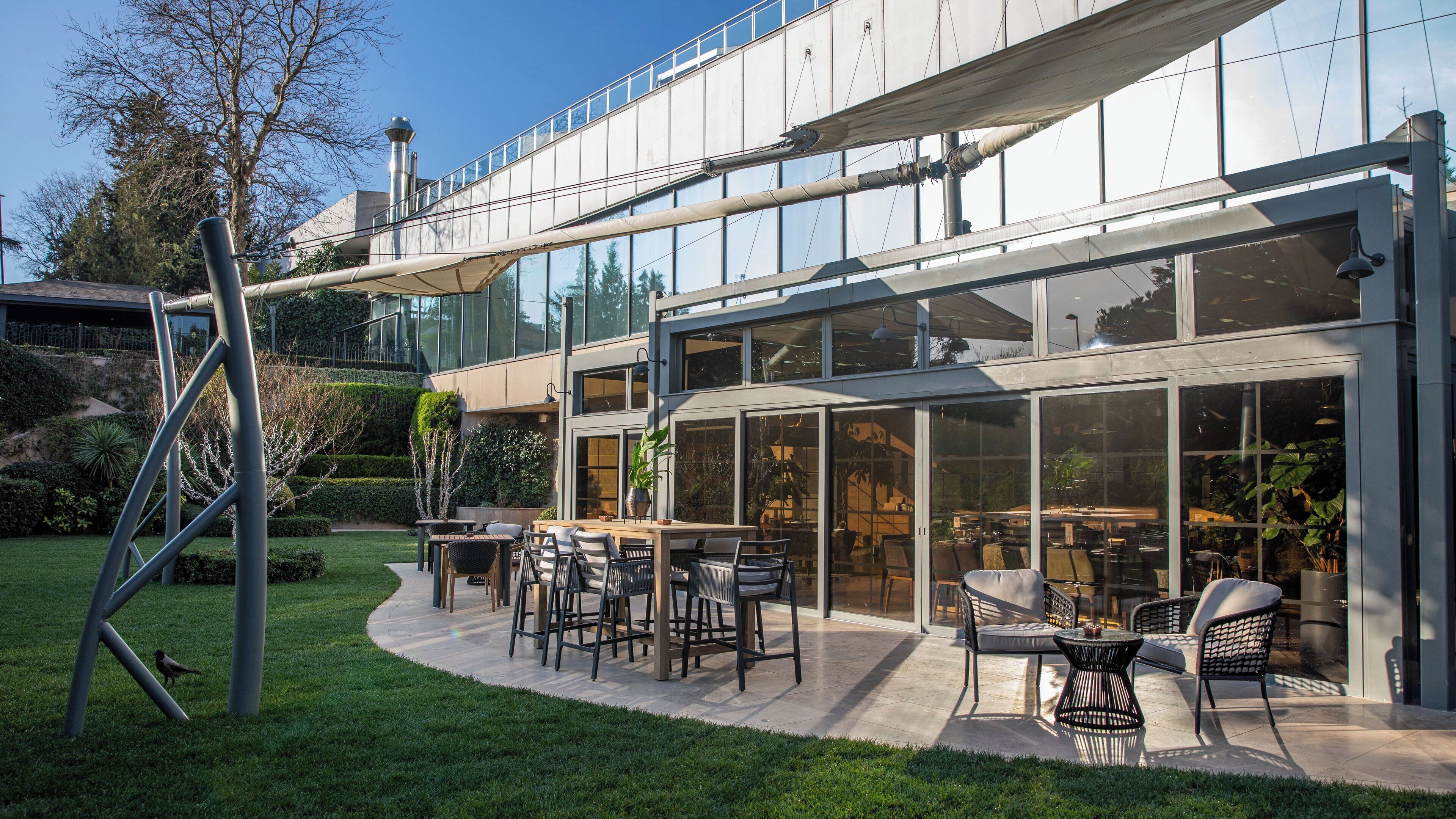 Een modern gebouw met een glazen gevel, een terras buiten en een goed onderhouden tuin.