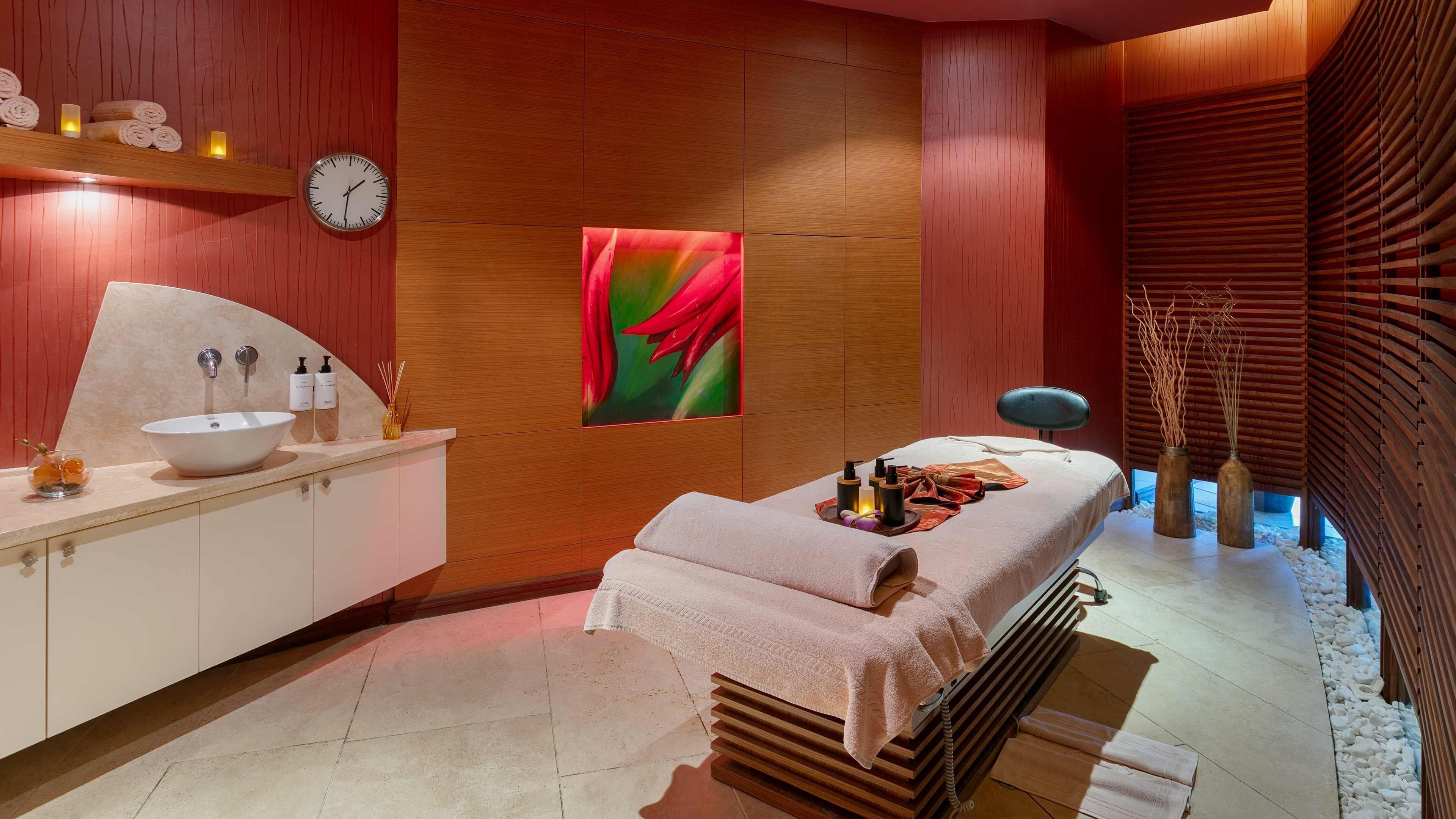 Ein moderner Spa-Bereich mit einem großen Waschbecken, einer Massageliege und einer Holzwand mit einer Uhr.