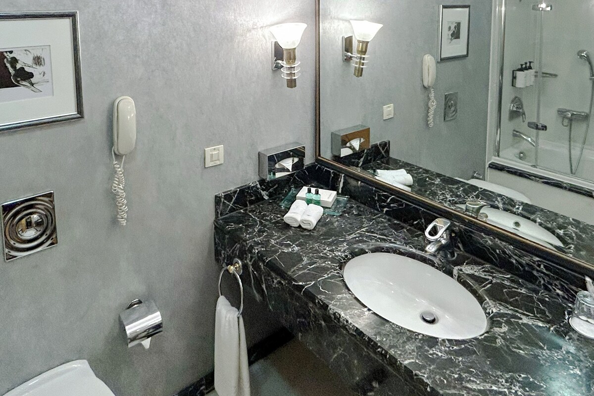 A bathroom with a marble sink, a mirror, a telephone, and a framed picture on the wall.