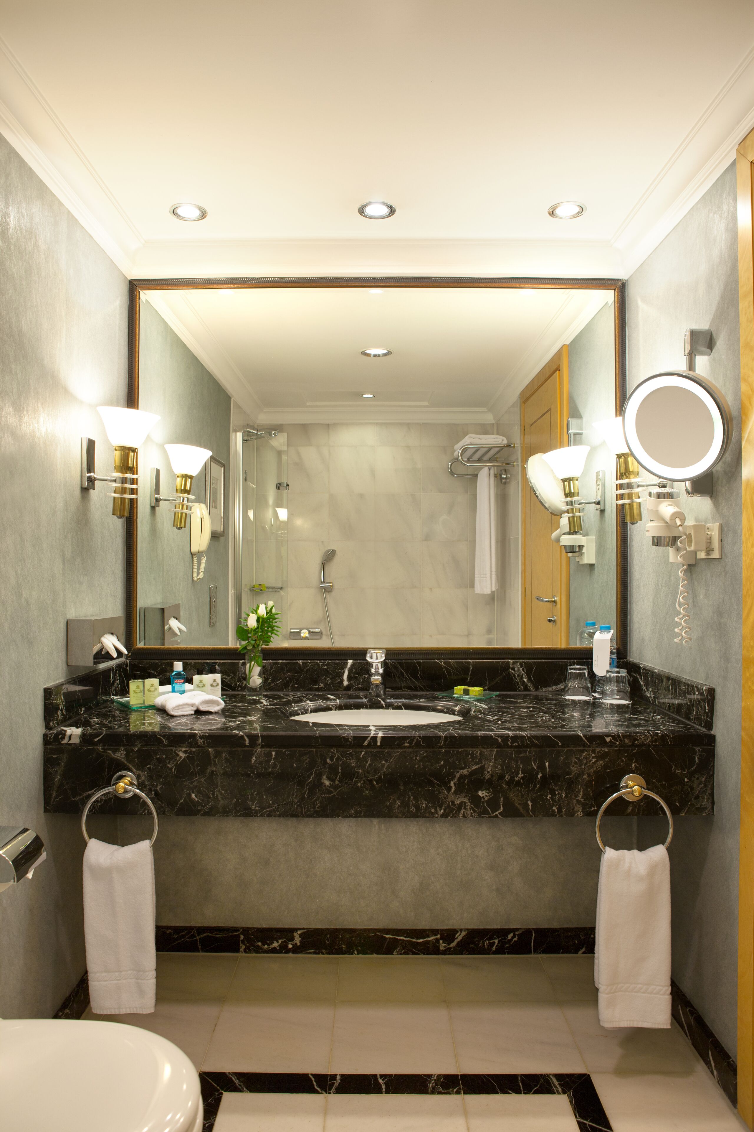 Un baño moderno con un lavamanos de mármol, dos toquilleros, un espejo grande y una ducha.