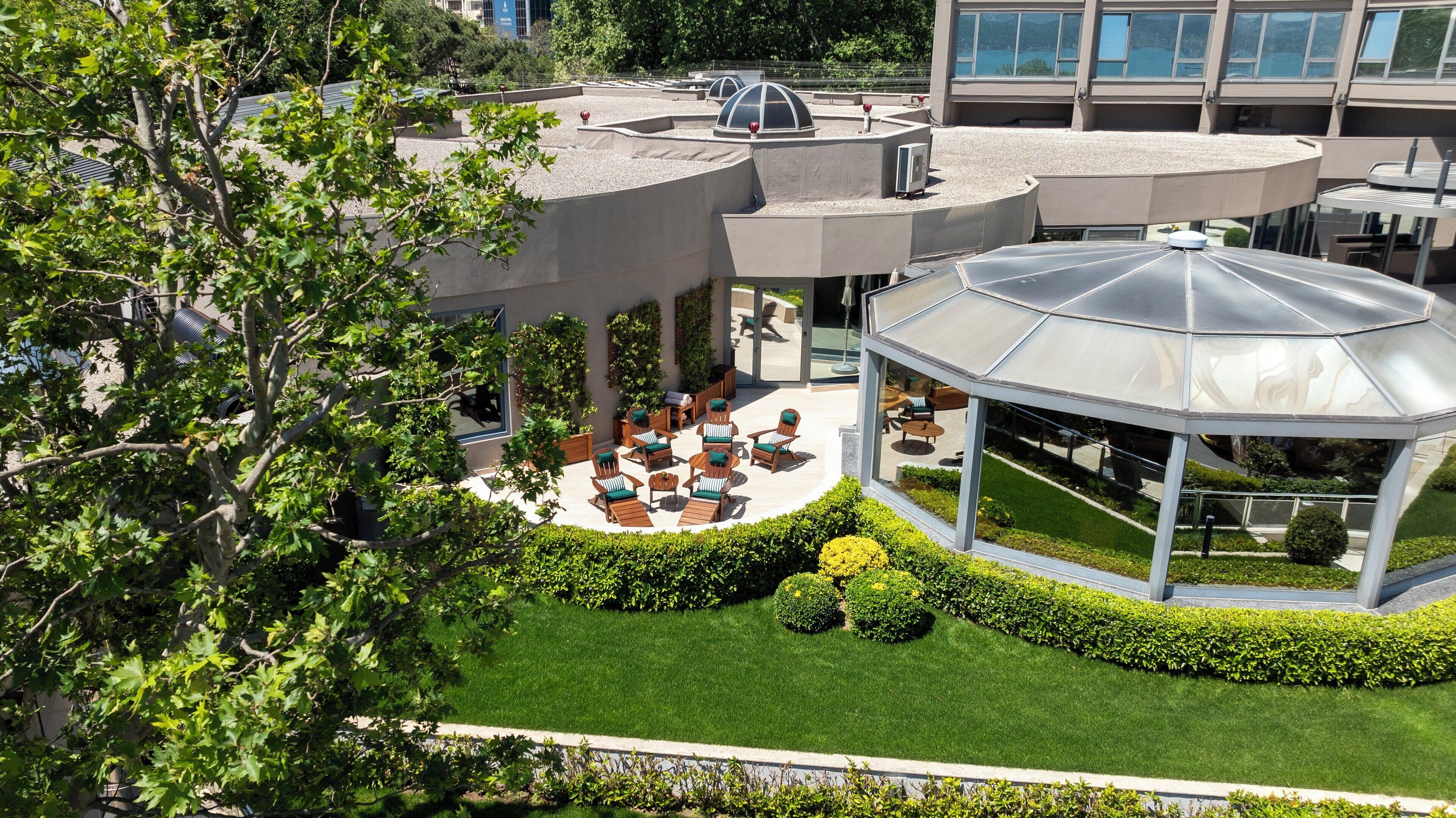 A modern outdoor lounge area with a glass gazebo, seating arrangements, and a well-maintained lawn.