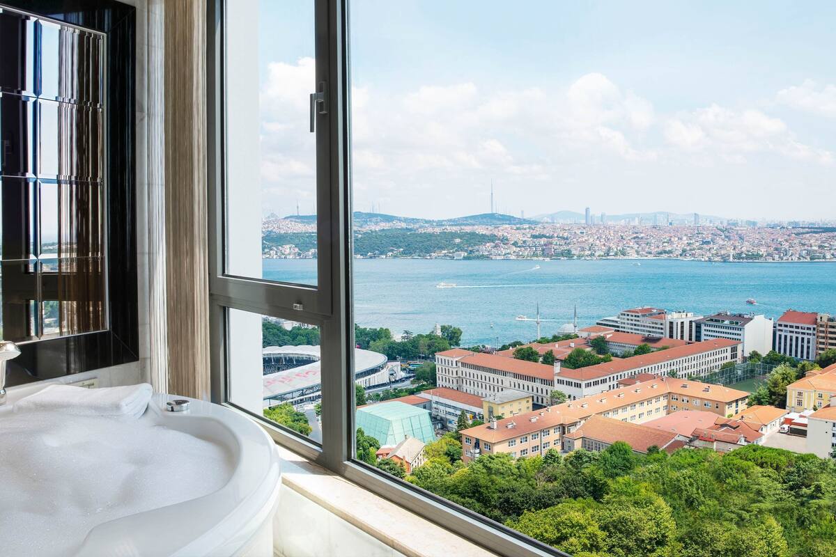 A bathroom with a large window offering a view of a cityscape and a body of water.