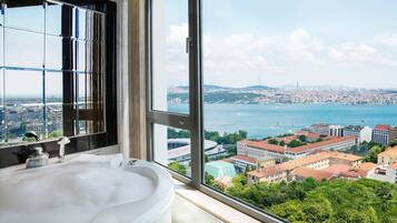 Un baño con un ventanal grande que ofrece vistas a un paisaje urbano y una masa de agua.