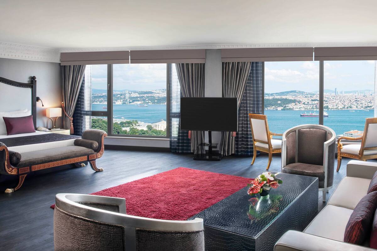 A hotel room with a large bed, a sofa, a TV, and a view of the sea.