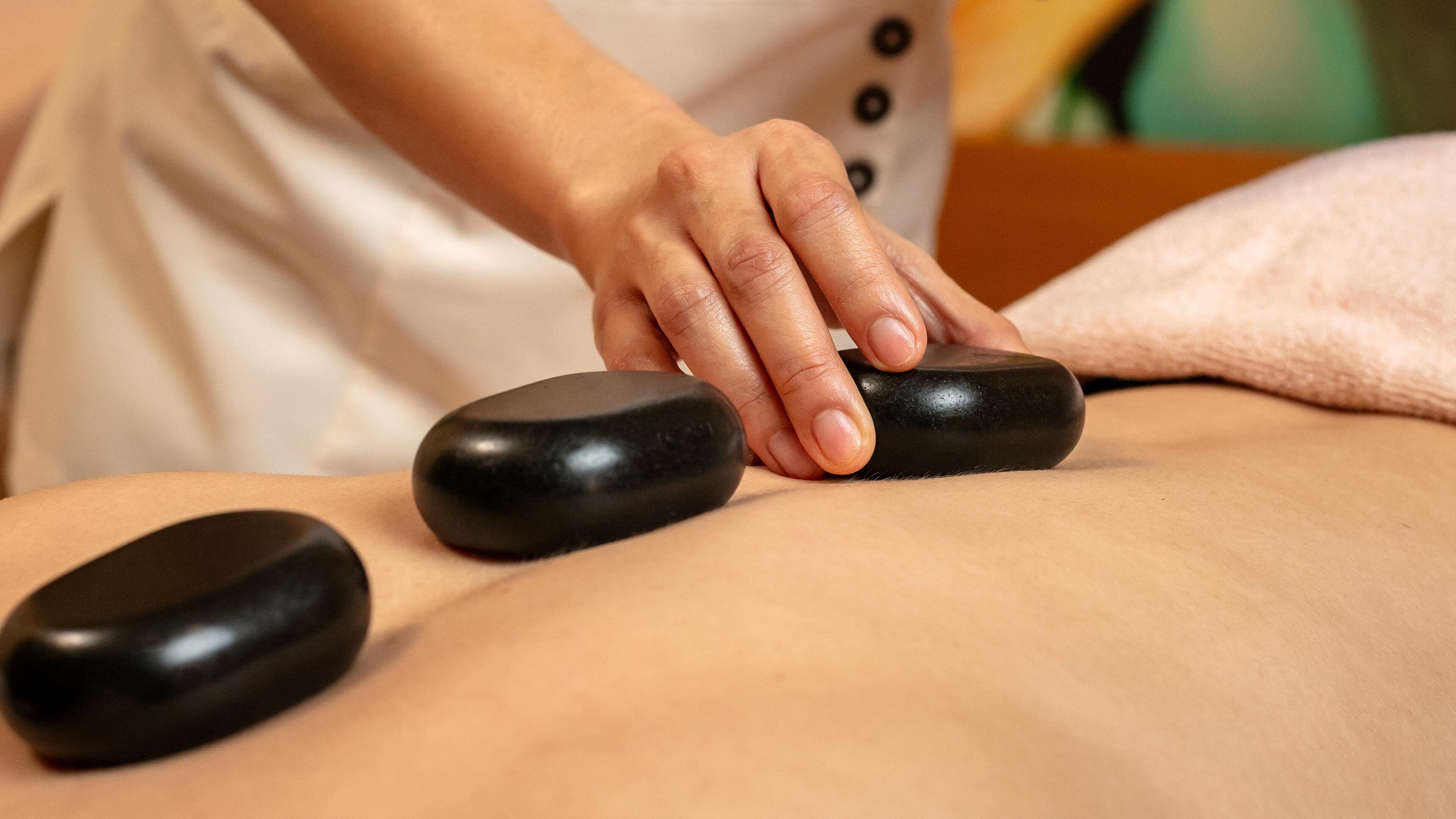 A massage therapy session with a person using a stone on another person's back.