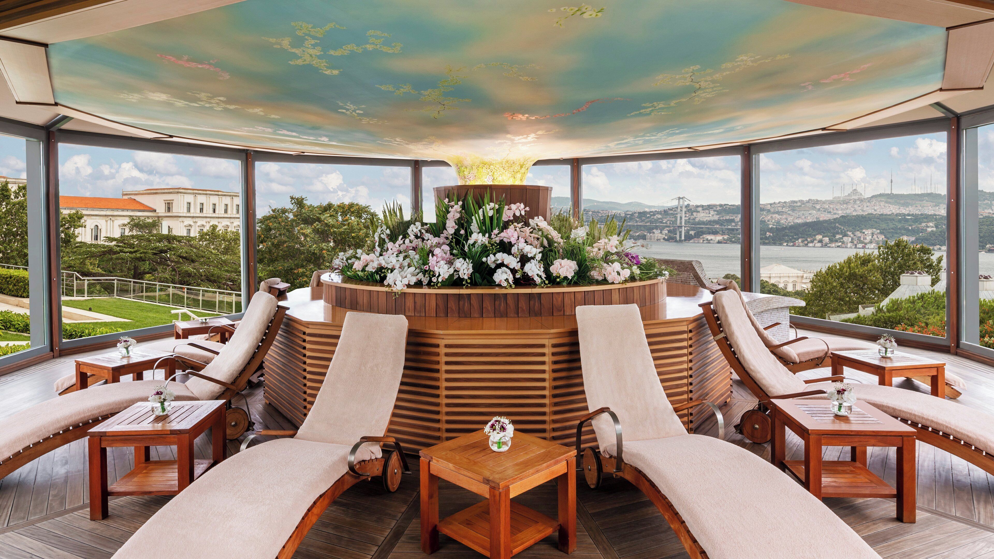 A high-ceilinged lounge with a central floral arrangement, multiple seating areas, and a view of a bridge and cityscape.