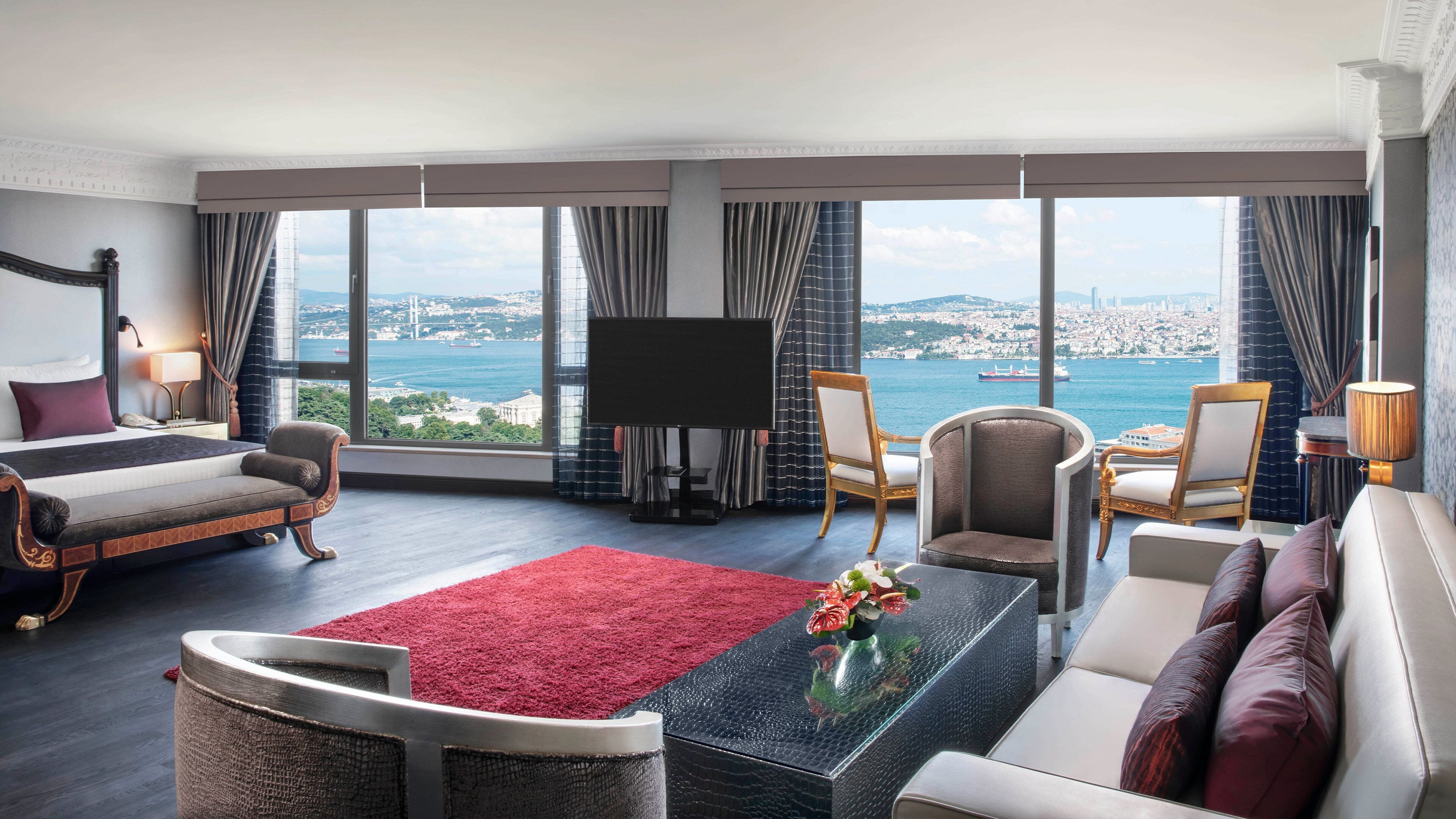 Habitación de hotel con una cama grande, un sofá, un televisor y vista al mar.