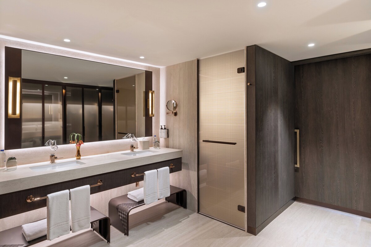 A modern bathroom with a large mirror, dual sinks, and a walk-in shower.