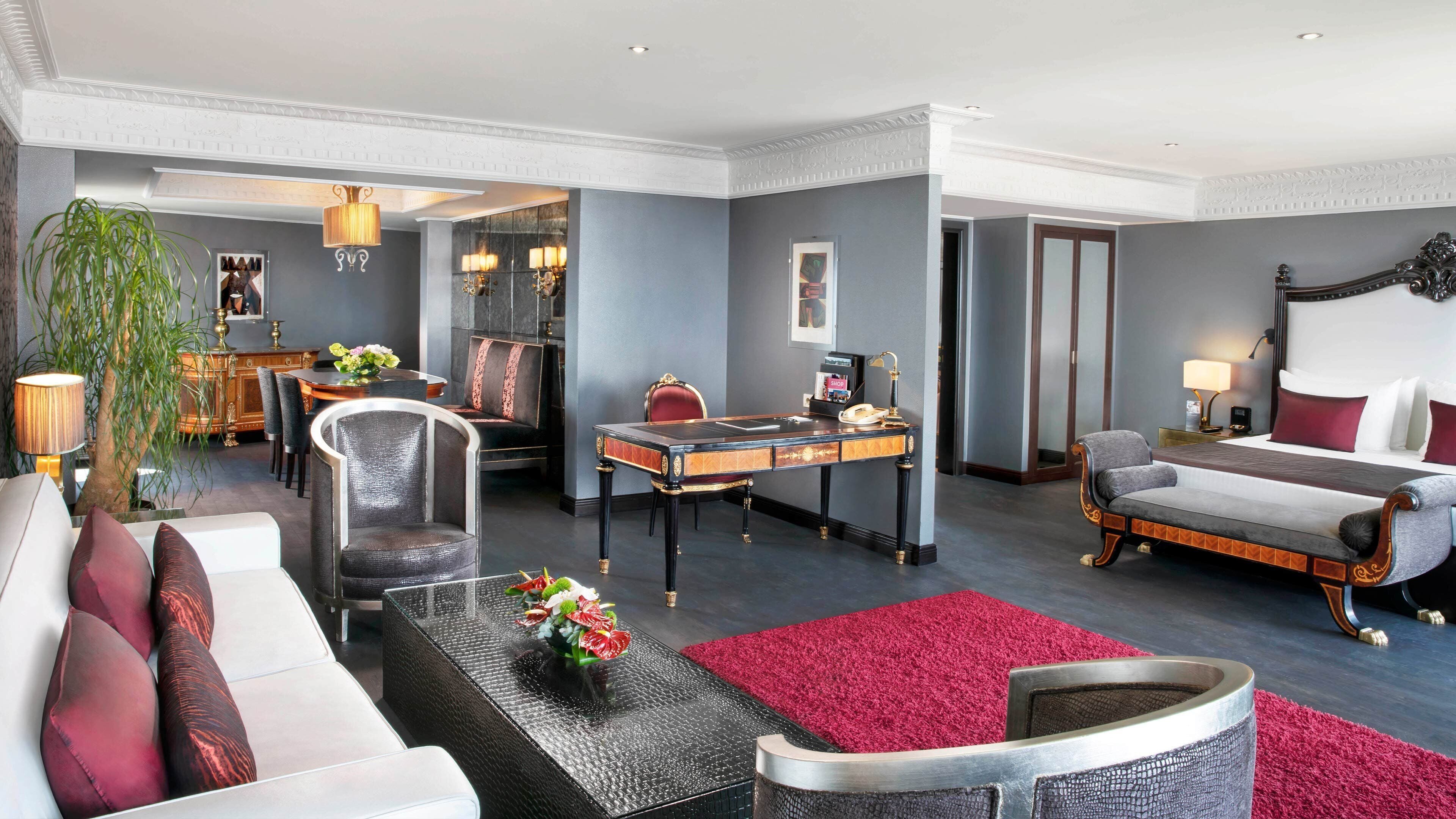 A hotel room with a dining area, a sofa, a desk, and a bed.