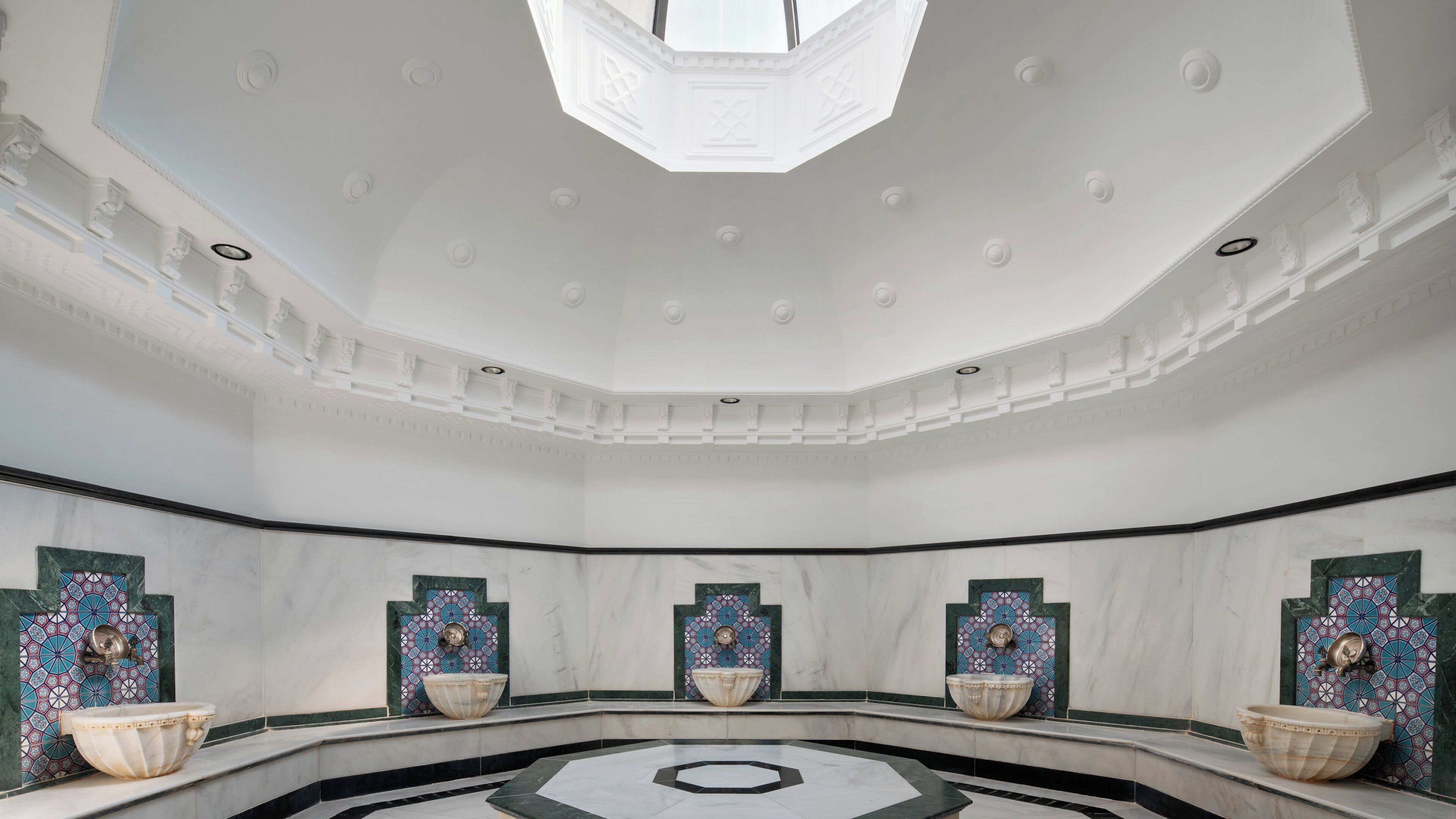 A spacious bathroom with a large central basin, decorative tiles, and a skylight.
