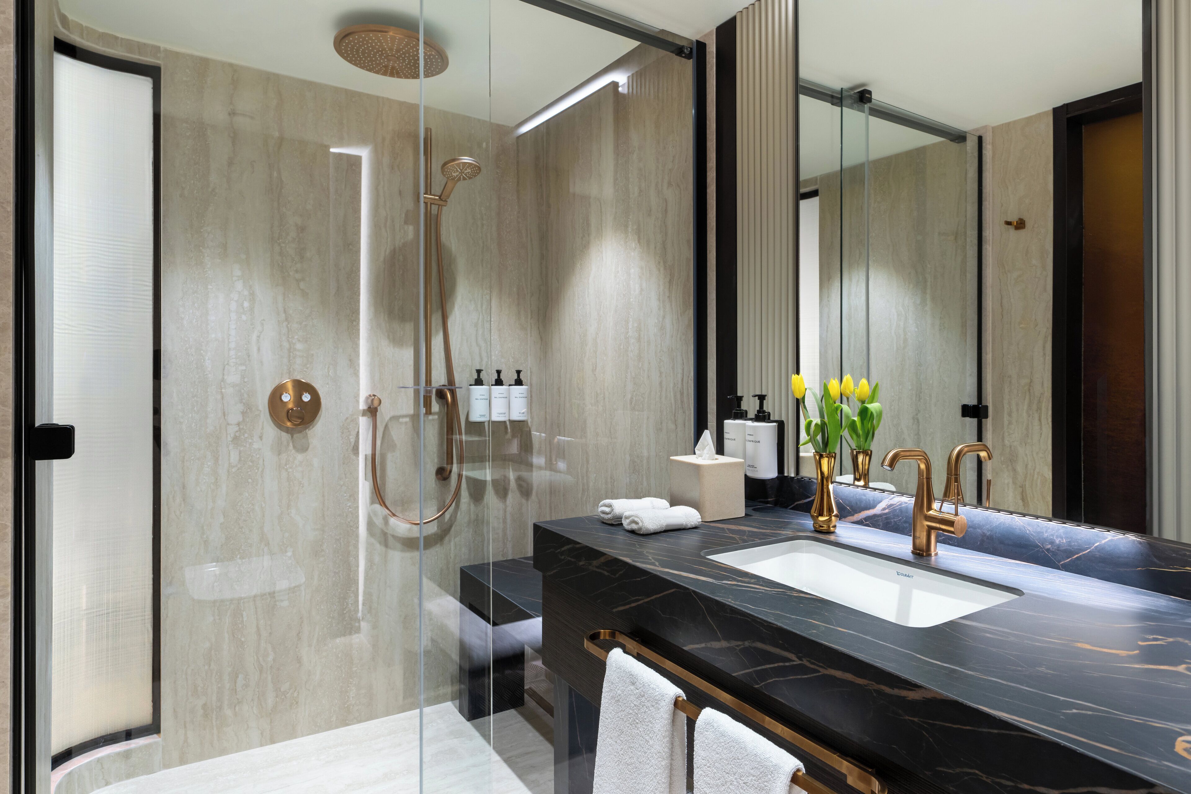 Un baño moderno con ducha envuelta en vidrio, lavamanos de mármol negro y un espejo grande.