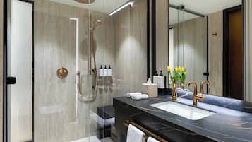 Un baño moderno con ducha envuelta en vidrio, lavamanos de mármol negro y un espejo grande.