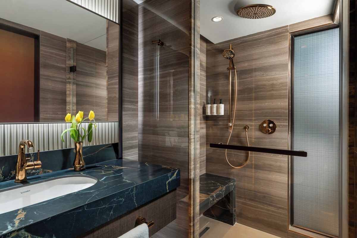 A modern bathroom with a marble sink, a glass shower enclosure, and a wooden vanity.