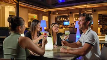 Un grupo de personas sentadas en una mesa en un restaurante, con una barra de bar al fondo.