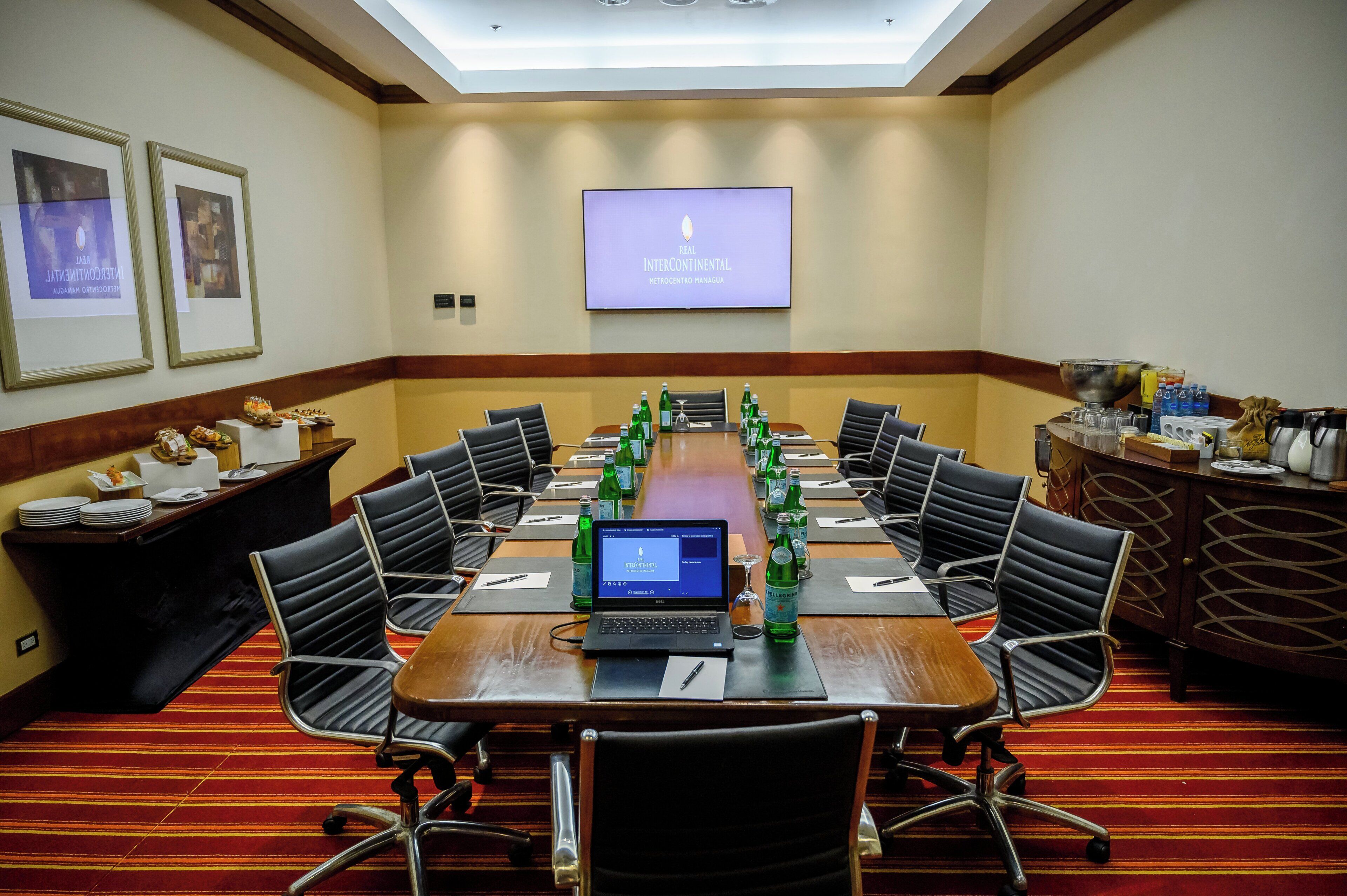 A conference room with a long table, chairs, a laptop, and a screen displaying 'REAL INTERCONTINENTAL METROCENTRO MANAGUA'.
