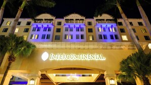 A hotel facade with illuminated signage, a grand entrance, and palm trees. - Real InterContinental Managua at Metrocentro Mall by IHG (Managua)