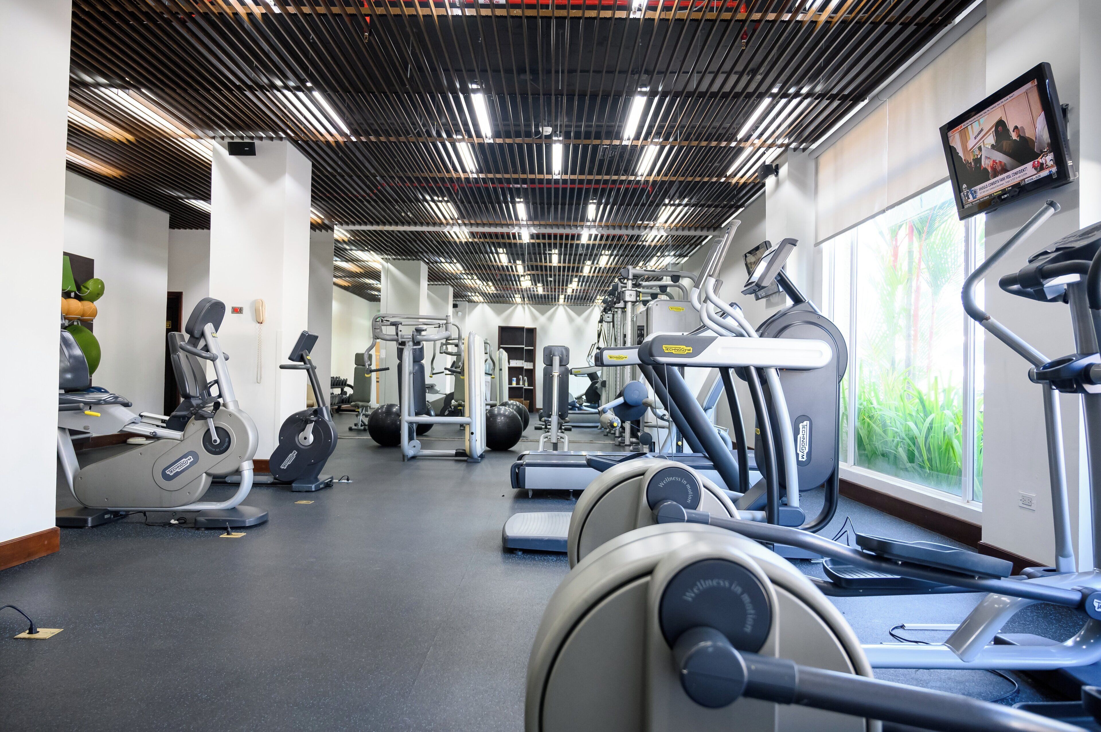 A gym with various exercise equipment, including treadmills and weight machines, and a large window providing natural light.