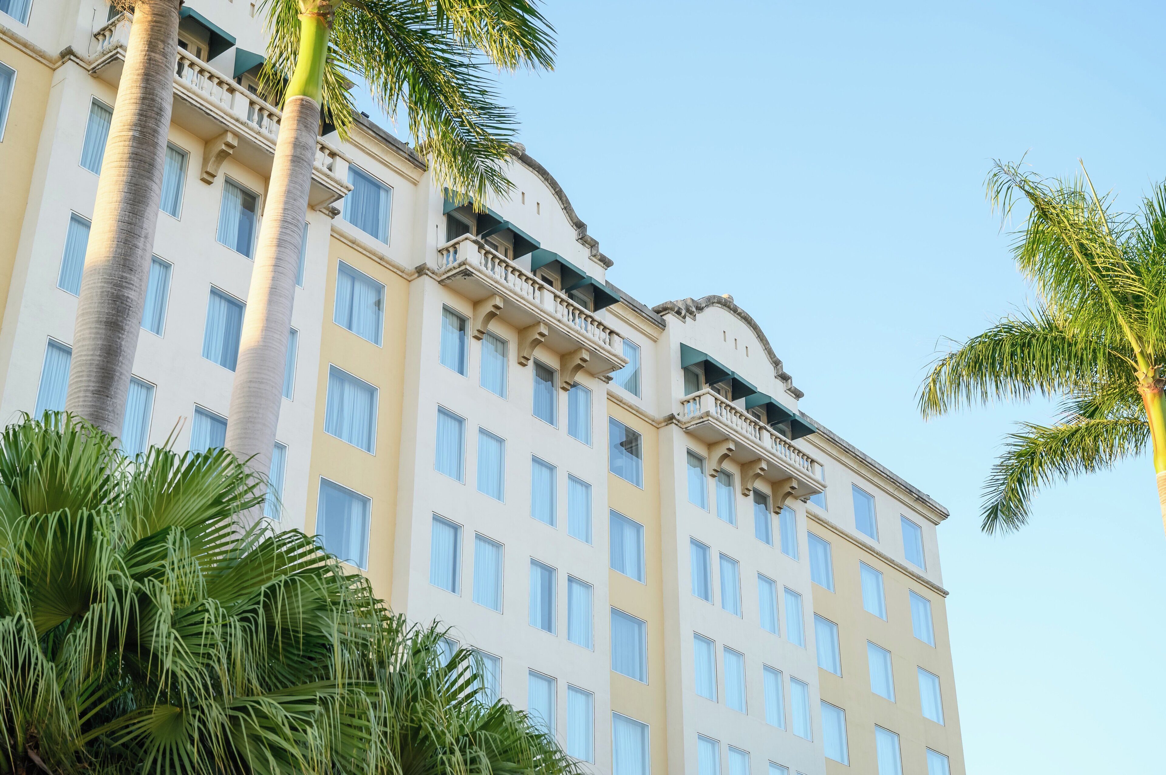 A multi-story hotel with balconies, large windows, and palm trees.