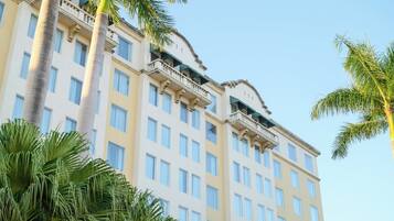 A multi-story hotel with balconies, large windows, and palm trees.