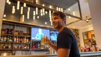 A man holding a beer glass in a bar with shelves of liquor bottles and a television screen in the background.