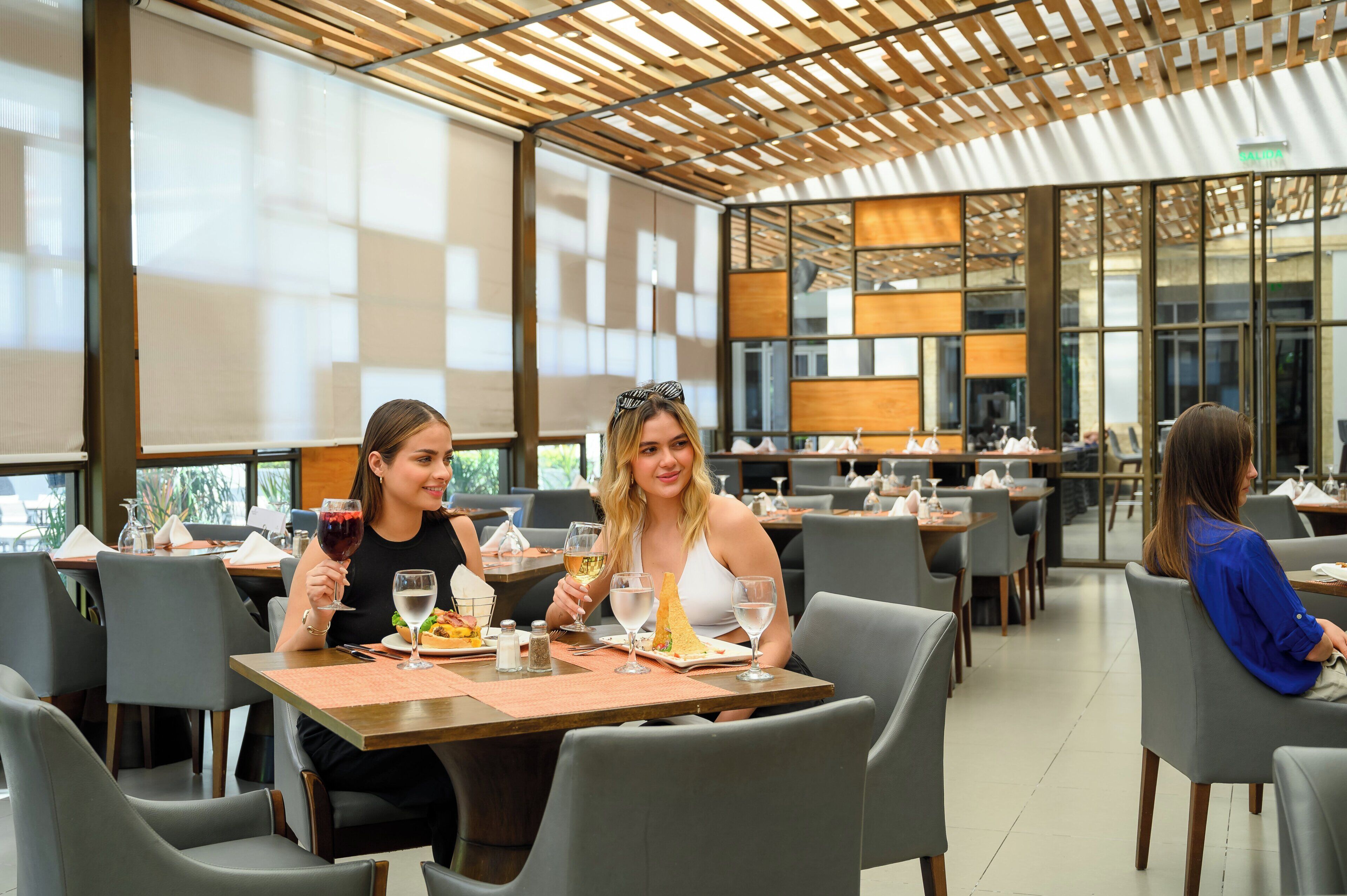 A modern restaurant with wooden ceiling panels, large windows, and a clean, organized layout.