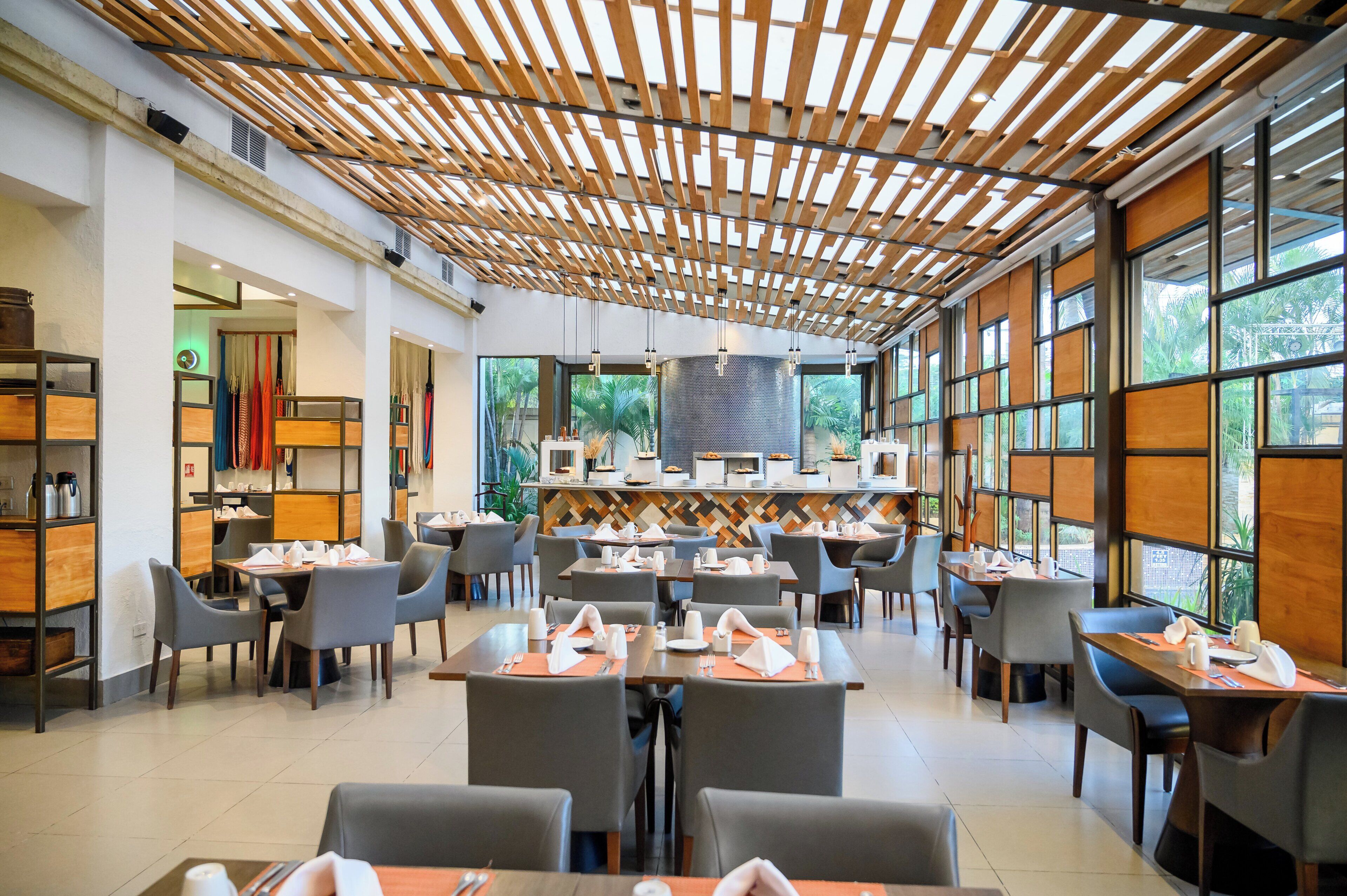 A modern restaurant with a wooden ceiling, large windows, and neatly arranged tables.