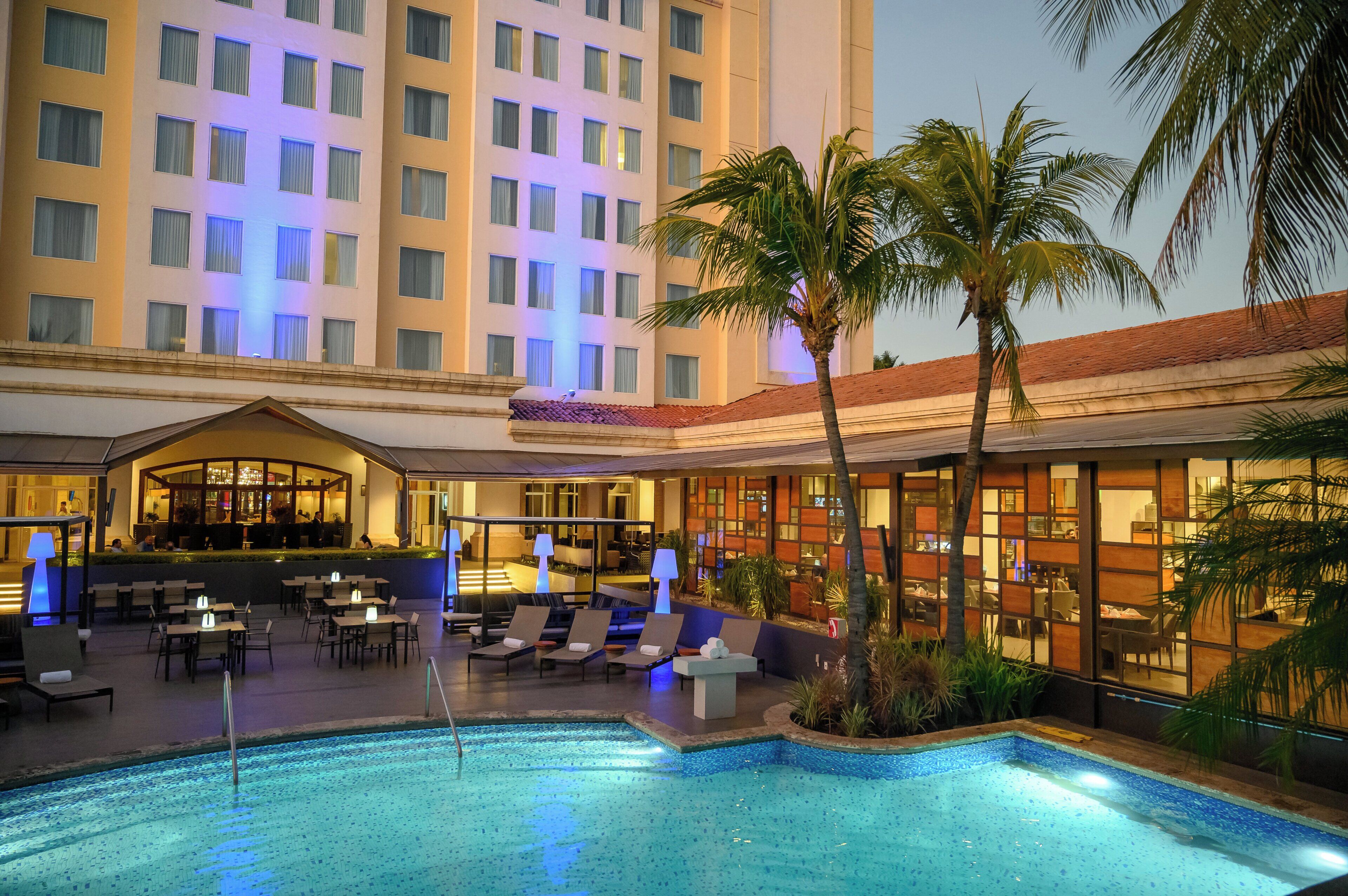 A hotel pool area with lounge chairs, a bar, and a restaurant.