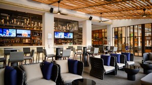 A modern bar area with multiple TVs displaying news, a variety of seating options including sofas and chairs, and a wooden ceiling design. - Real InterContinental Managua at Metrocentro Mall by IHG (Managua)