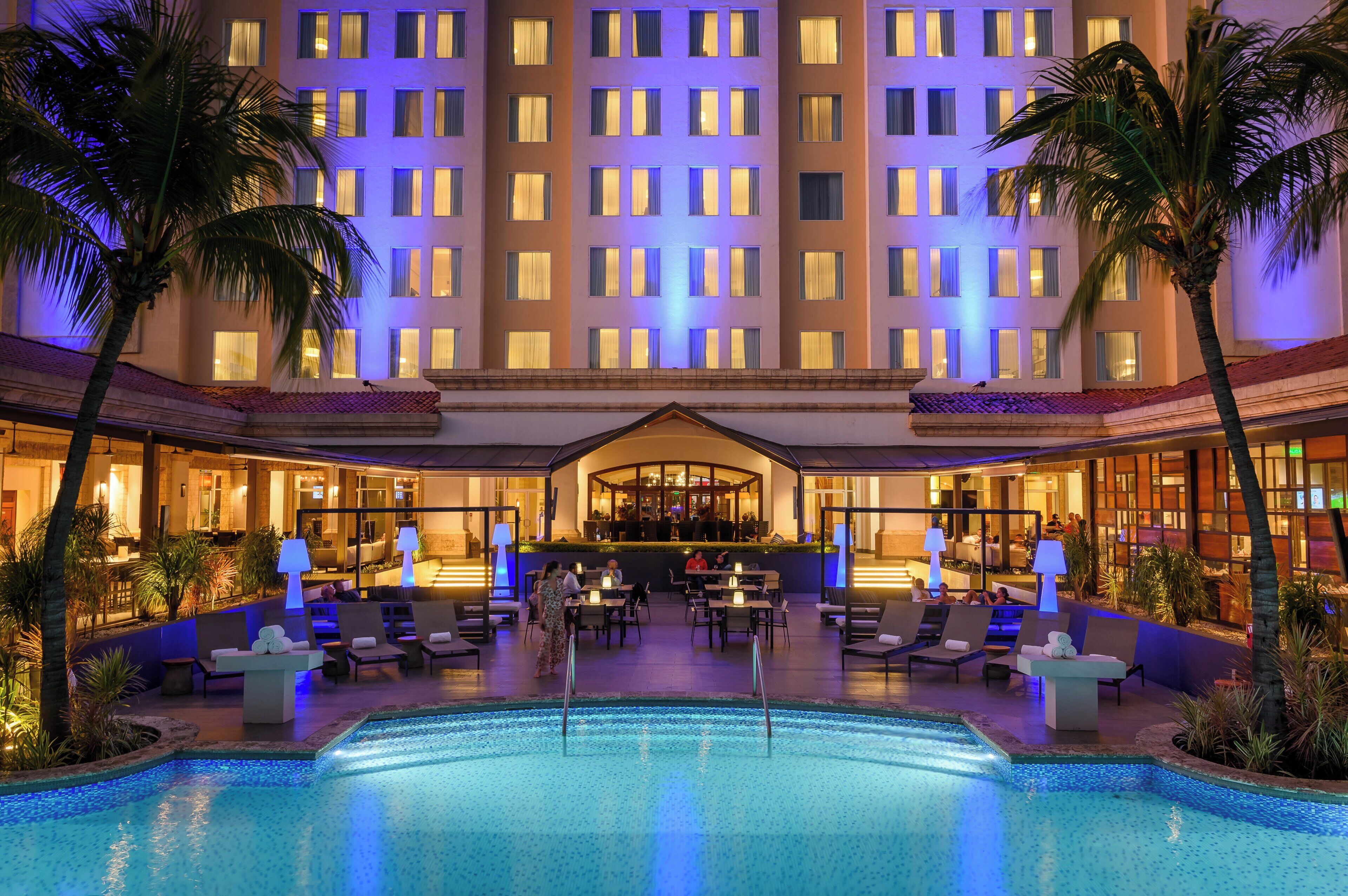 A hotel with a pool, lounge area, and bar.