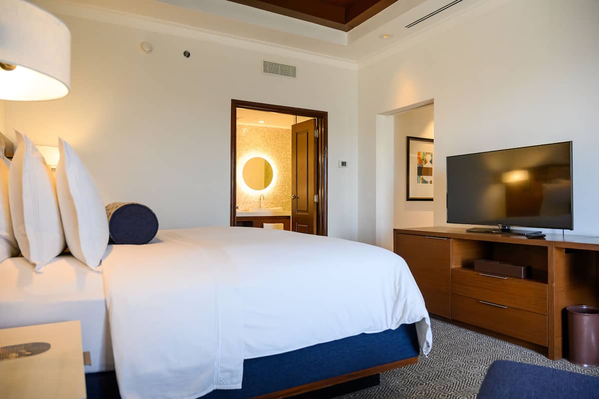 A hotel room with a bed, a TV, a desk, and a bathroom with a mirror and sink.