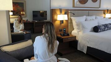 Quarto de hotel com cama, abajures, televisão, escrivaninha e sofá.