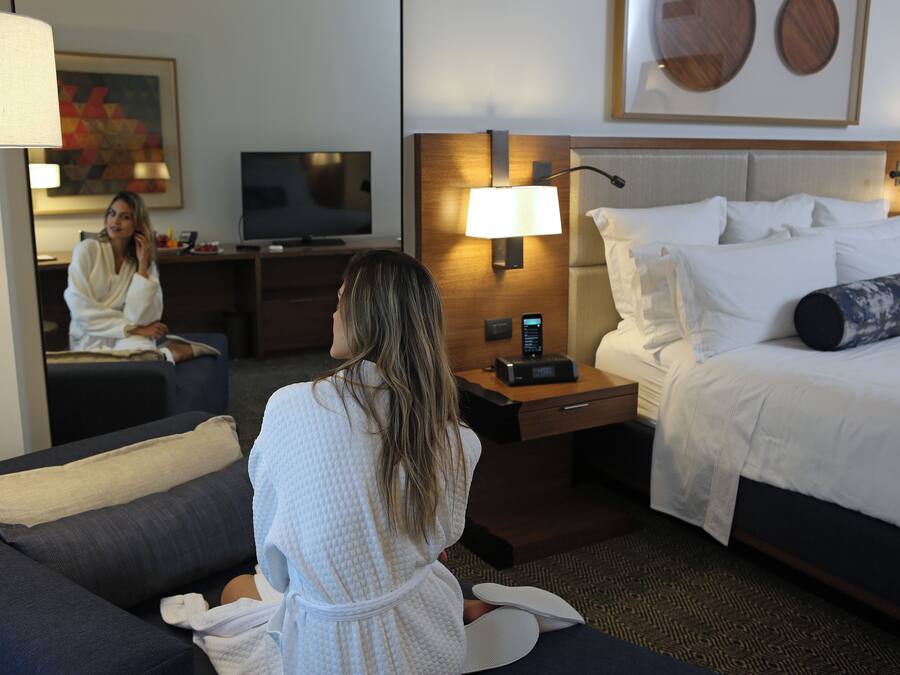 Quarto de hotel com cama, abajures, televisão, escrivaninha e sofá.