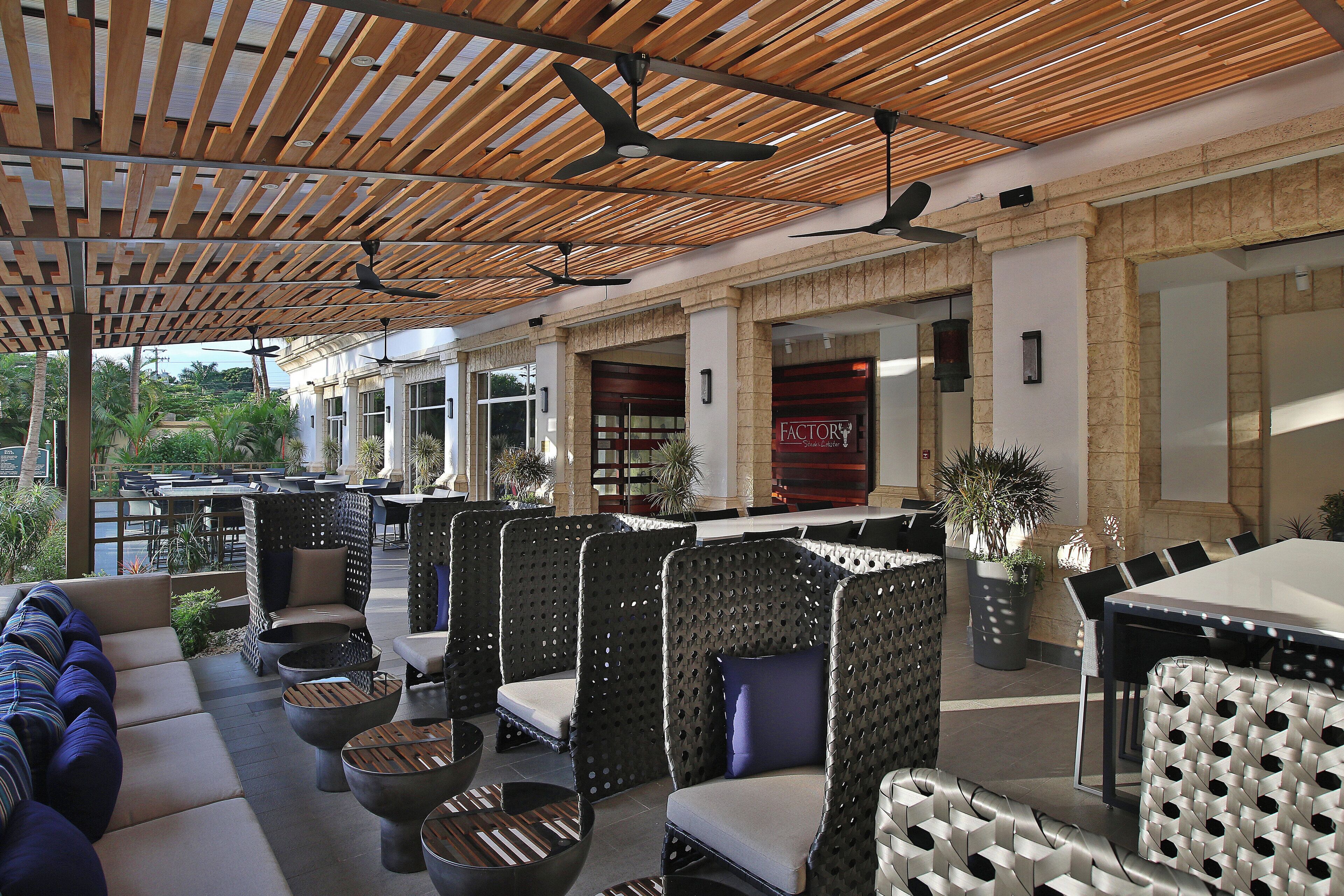 An outdoor seating area with wicker furniture, a ceiling fan, and a view of a restaurant named 'FACTOR Steakhouse'.