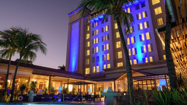 A hotel with a pool, palm trees, and a well-lit facade. - Real InterContinental Managua at Metrocentro Mall by IHG (Managua)