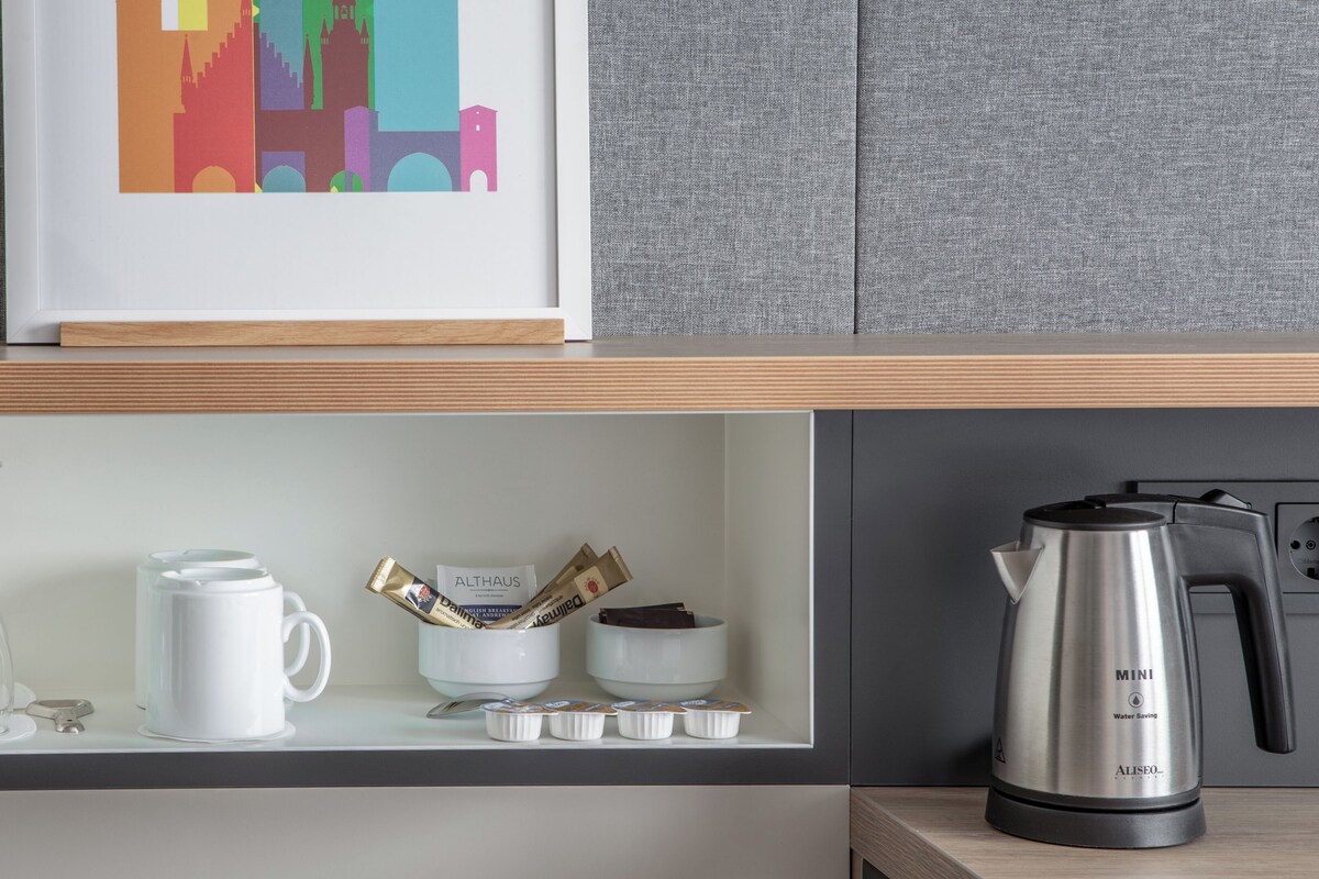 A kitchen counter with a coffee maker, a framed cityscape picture, and a set of white cups and a glass.